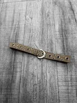 Cinto de gamuza color beige con hebilla metálica plateada y ojalillos metálicos.