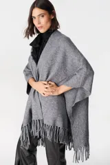 Ruana gris de tejido suave y envolvente, con diseño abierto y terminaciones con flecos en el ruedo.
