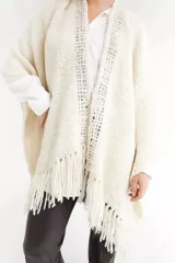 Ruana color crema tejida a mano, con cuello redondo y flecos en el ruedo.