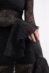 Vestido largo de encaje negro con transparencias, corte ajustado al cuerpo, mangas largas con terminación acampanada y falda con caída fluida.