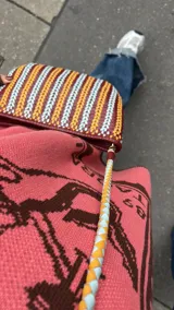 Cartera de mano tipo clutch, de cuero trenzado a mano en color negro y beige, con diseño de rayas verticales.