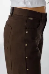 Jean de corte recto y tiro medio, color azul, con detalles de tachas metálicas doradas a lo largo de las costuras laterales externas.