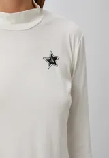 Polera blanca de tejido de punto fino, con cuello alto y manga larga. Tiene un pequeño logo de estrella bordado en el pecho.