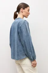 Camisa de jean de corte clásico con cuello mao, cierre frontal con botones y mangas largas abullonadas con puños elásticos.