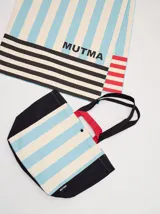 Bolso tipo tote con diseño de rayas verticales en amarillo y blanco, con laterales, base y correas en color marrón. Incluye asas cortas en color naranja y cierre con botón a presión.