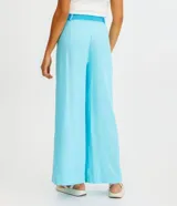 Pantalón acampanado de lino color celeste, con bolsillos, cinturón bordado y pliegues delanteros.