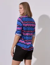 Camisa de manga 3/4 con estampado zig zag en tonos azul, rosa y negro. Tiene cuello con solapa, escote en V, abertura central con botones y bolsillo simulado en el pecho.