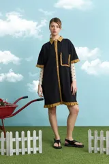 Túnica de algodón color negro, con cuello polo, manga corta, cartera frontal con botones y bolsillo ojal en el pecho. Presenta detalles de voladitos mostaza en el cuello, la botonera, los puños, el bolsillo y el ruedo.