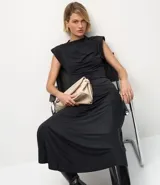 Vestido midi negro sin mangas, con cuello alto y sisa amplia. Presenta fruncidos delanteros que crean un efecto drapeado en la falda.
