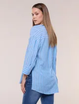 Blusa de silueta holgada a rayas verdes y blancas, confeccionada en tela liviana con textura arrugada. Presenta cuello en V profundo con botones frontales, mangas 3/4 de hombro caído y ruedo asimétrico con aberturas laterales.