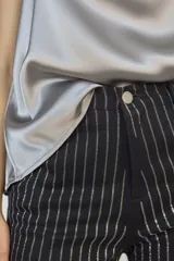 Jeans de corte recto en color negro, con diseño de rayas verticales formadas por aplicaciones de strass plateado. Presenta tiro medio-alto, cierre frontal con botón y bolsillos laterales.