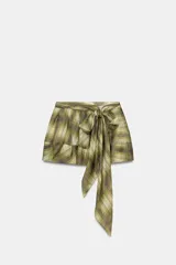 Falda corta de tiro medio con estampado de cuadros en tonos verdes y beige. Presenta un detalle de cinturón tipo lazada confeccionado en el mismo tejido y cierre lateral con cremallera oculta en costura.