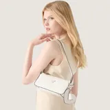 Cartera tipo baguette Guess modelo Isobel, color blanco con acabado texturizado. Presenta herrajes en tono dorado, logo triangular frontal y un charm colgante en forma de corazón. Incluye cierre superior y correa ajustable.