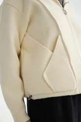 Abrigo negro con capucha, confeccionado en tejido de textura suave. Presenta cierre frontal con cremallera, bolsillos laterales integrados con costuras decorativas y puños ajustados.