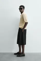 Polo de punto con estructura calada en color beige, confeccionado en algodón. Presenta un calce relajado, manga corta, cuello solapa con abertura frontal y terminaciones acanaladas.