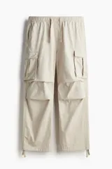 Pantalón cargo color beige de corte ancho, con cintura elástica ajustable con cordón, bolsillos laterales, traseros y tipo cargo con solapa y botón a presión en las piernas. Cuenta con cordón ajustable en los bajos.