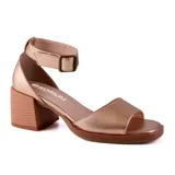 Sandalias de cuero sintético color hueso, con punta descubierta, tira ancha sobre los dedos, pulsera al tobillo con hebilla metálica y taco geométrico color madera clara.