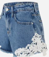 Short de jean tiro medio con encaje floral blanco aplastado en los laterales y dobladillo deshilachado. Cuenta con bolsillos delanteros y traseros, pasacintos y cierre frontal con botón y cremallera.