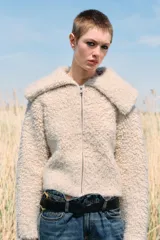 Chaqueta de punto bouclé color crudo, con cuello de solapa grande, manga larga y cierre frontal con cremallera.