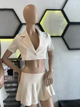 Conjunto de dos piezas color beige compuesto por un blazer corto de manga corta con cierre frontal de un botón y una pollera tableada de tiro bajo.