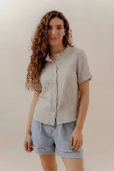 Camisa de manga corta color beige, con cuello fruncido y cierre frontal de botones.