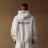 Hoodie de algodón y poliéster color gris jaspeado, con capucha, bolsillo canguro frontal y estampado en la espalda con el texto "ESSENTIALS FEAR OF GOD".