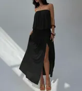 Vestido largo color beige, sin tirantes, con escote recto y detalle fruncido en la cintura. La falda es fluida y tiene una abertura lateral.