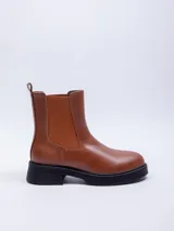 Bota corta color marrón de cuero sintético, con elásticos laterales y suela track color negro.