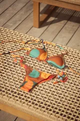Bikini con estampado de círculos en tonos marrones, naranjas y turquesas. El top es de triángulos movibles con almohadillas desmontables y se ata al cuello y espalda. El bottom es vedetina con tiritas ajustables a los costados.