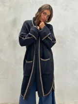 Saco largo de punto color negro, con cuello alto, mangas largas y detalles de ribetes beige en los bordes, puños y bolsillos.