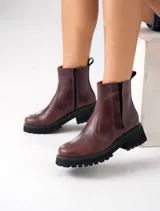 Botas Kiev de cuero vacuno color marrón, con suela de goma negra tipo track. Tienen cierre YKK en el lado interno y elástico en el lado externo. La punta es redonda y ancha.