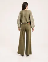 Pantalón de pana color verde oliva, de corte wide leg y largo al tobillo. Tiene cierre delantero con botón, bolsillos laterales y traseros.