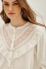 Camisa de manga larga color negro, con cuello redondo y cierre frontal de botones. Presenta un diseño con volados en la parte superior delantera y detalles de encaje bordado en los hombros y pecho.