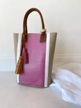 Bolso matero color fucsia con textura croco, laterales color beige con borde blanco y manijas de cuero marrón.