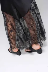 Vestido largo de seda color rojo, con escote en V y breteles finos. Presenta detalles de encaje en el escote y un diseño asimétrico en la falda que incorpora encaje transparente desde la altura de la rodilla.