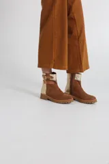 Bota estilo biker de caña media, confeccionada en cuero negro con detalles en gamuza marrón. Presenta correas ajustables con hebillas metálicas, tachas decorativas y suela track dentada.