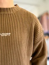 Sweater de punto color marrón, de manga larga, con textura acanalada y texto bordado en la espalda.