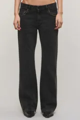 Jeans de denim negro de tiro medio y corte bootcut, con tachas metálicas doradas a lo largo de los laterales y en los bolsillos delanteros.