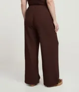 Pantalón de tiro alto, corte flare (acampanado), color marrón oscuro, confeccionado en tejido texturizado anarruga con cintura elástica.