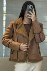 Campera tipo gamulán de color crema con interior y cuello de corderito sintético. Presenta cierre frontal cruzado, bolsillos laterales con cierre y detalles de costuras en contraste color marrón oscuro.