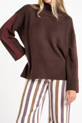 Polera de punto con calce oversize, cuello alto y mangas largas. Presenta un diseño en color negro con franjas laterales en las mangas y detalle en el cuello en tono bronce con acabado brillante.