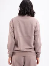Buzo de felpa color beige, con cuello alto y cierre frontal parcial, de manga larga con puños elásticos.