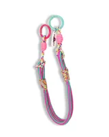 Correa para bolso de diseño moderno, confeccionada con cuerda trenzada en colores vibrantes fucsia y verde. Presenta detalles de nudos decorativos, dos argollas metálicas en los extremos (una fucsia y una turquesa) y una etiqueta colgante con logo.