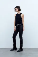 Pantalón jean negro engomado, corte slim, con tajo en el ruedo y cintura con cinturón de cuero con tachas.