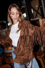 Chaqueta de gamuza marrón con diseño de flecos en la parte delantera y las mangas, corte tipo camisa y cierre frontal de botones.