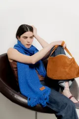 Cartera de hombro confeccionada en gamuza color tostado, con diseño de silueta curva y cierre superior. Cuenta con una correa fija y un acabado suave al tacto.