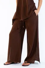 Pantalón ancho de color marrón, con pretina elástica, bolsillos laterales y aberturas en los bajos. Confeccionado en tejido fluido.