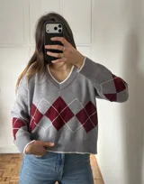 Sweater de punto con diseño de rombos en color gris, bordó y blanco. Presenta cuello en V con detalle de borde en contraste, mangas largas y puños acanalados.