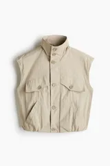 Camisa cargo sin mangas de nylon color beige, con cuello alto, cierre frontal de botones, bolsillos superiores con solapa y bolsillos delanteros diagonales. Cuenta con elástico oculto en el bajo.