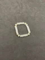 Pulsera elástica compuesta por cuentas de vidrio traslúcido en tono blanco y pequeños separadores metálicos dorados.